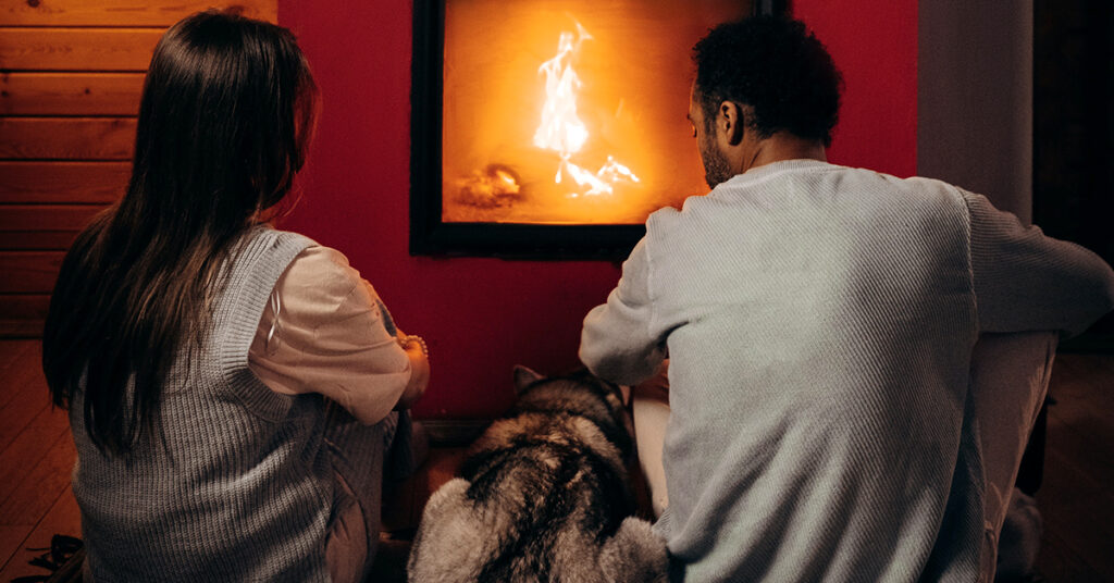 Woman, Dog, and man sitting in front of a fireplace.