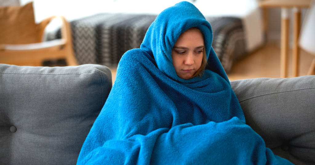 cold woman wrapped up in blanket on couch