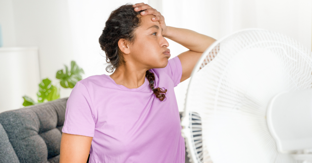woman sitting in front of fan because of HVAC system isn't working